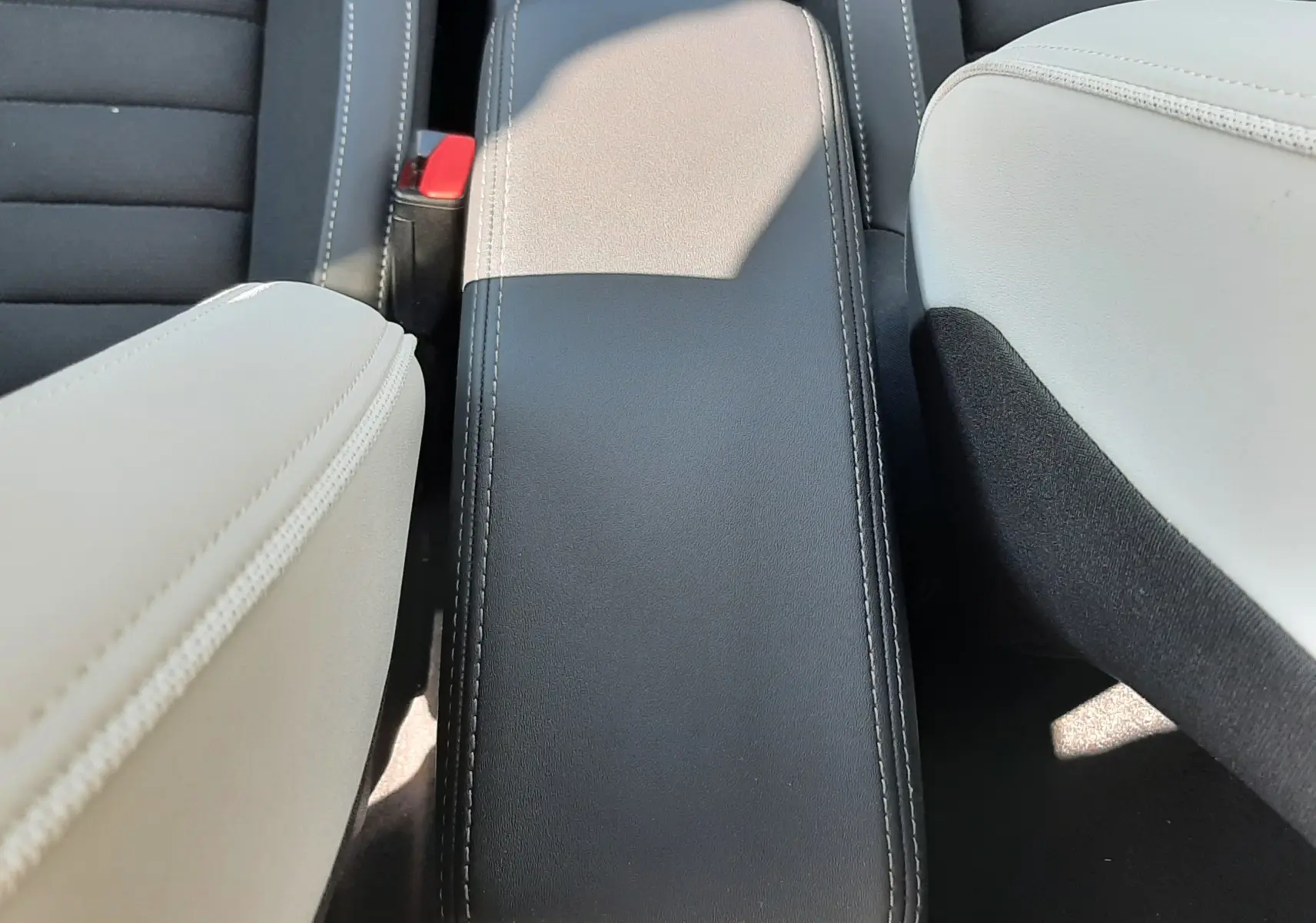 Vue rapprochée de l'accoudoir central noir entre les sièges avant en cuir clair du Citroën C3 Aircross 2025 hybride.