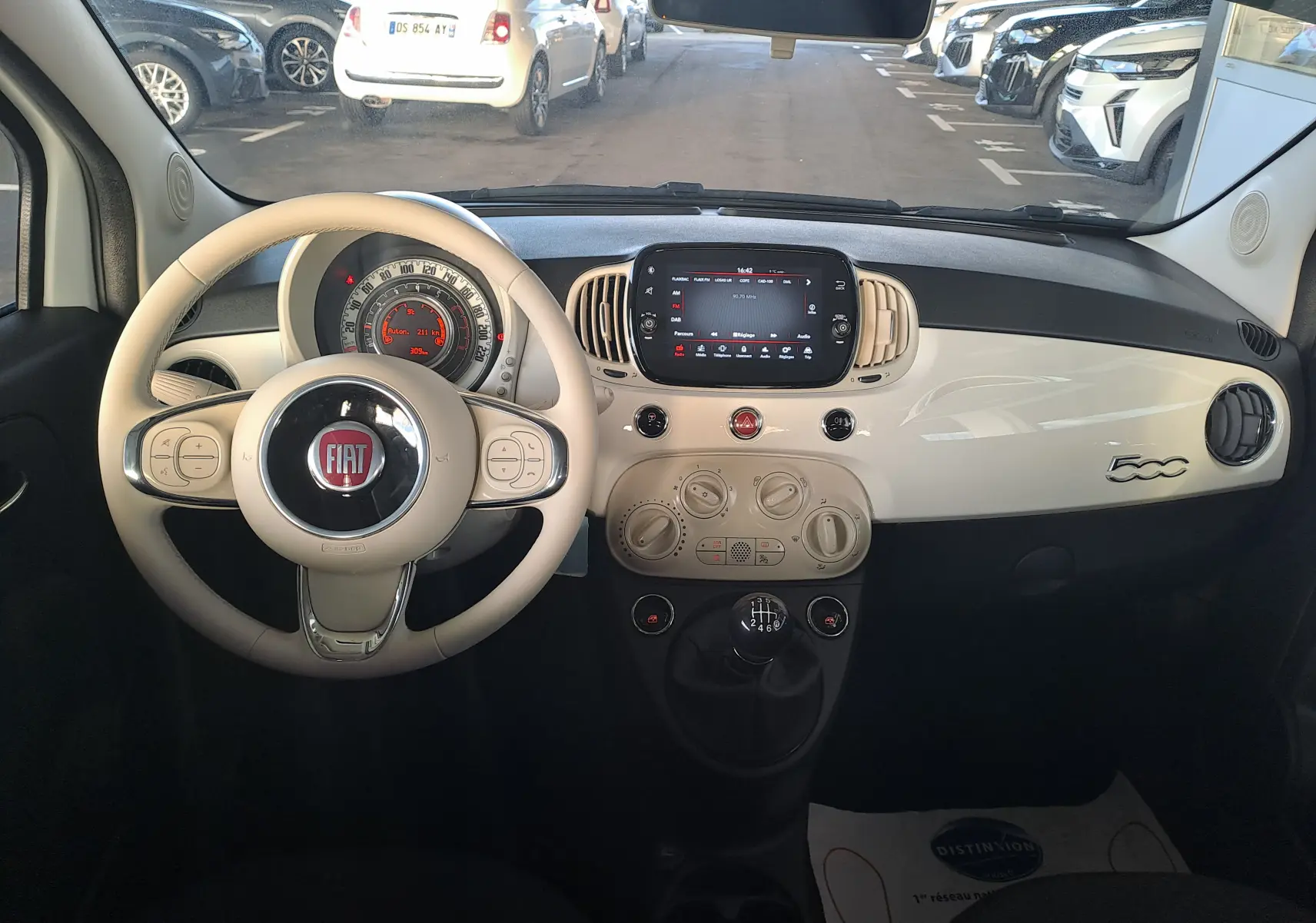 Intérieur de la Fiat 500 2023 en blanc, vue du poste de conduite avec volant beige et tableau de bord compact.