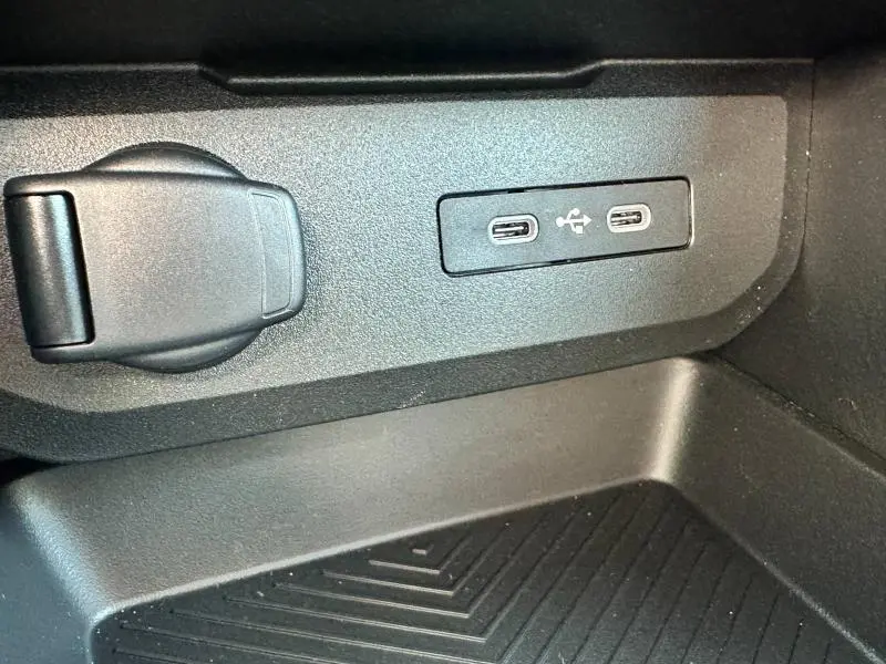 Prise USB double et prise 12V noire en gros plan dans le compartiment intérieur d'une Dacia Bigster blanche.