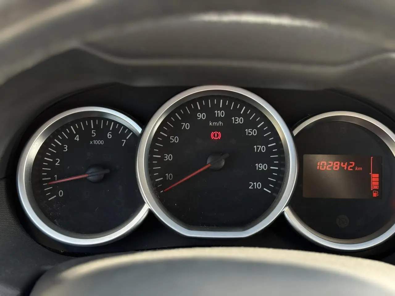 Gros plan sur le tableau de bord du Dacia Duster blanc, affichant le compteur et l'odomètre à 102842 km.