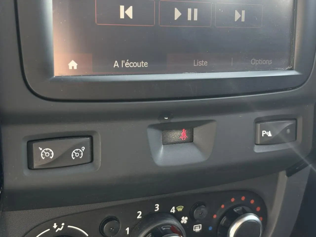 Gros plan sur la console centrale du Dacia Duster blanc, montrant les commandes de régulateur, alerte ceinture et radar de recul.