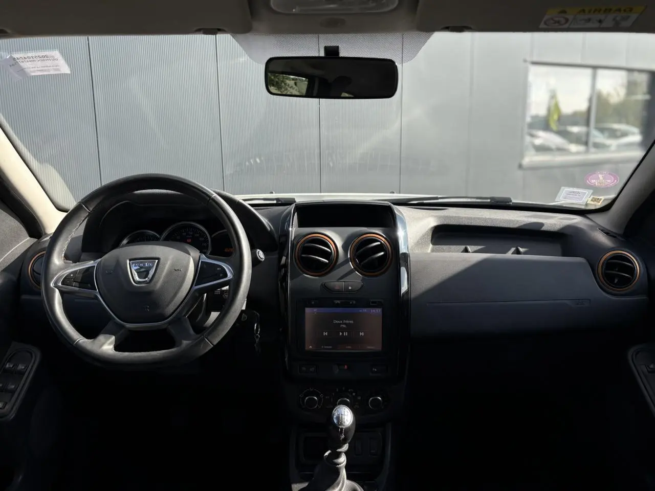 Vue frontale de l'intérieur du Dacia Duster blanc glacier 2017, volant cuir et écran GPS tactile au centre.