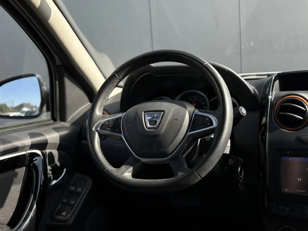 Vue rapprochée du volant en cuir noir du Dacia Duster TCE 125 Explorer, avec commandes multifonctions visibles.