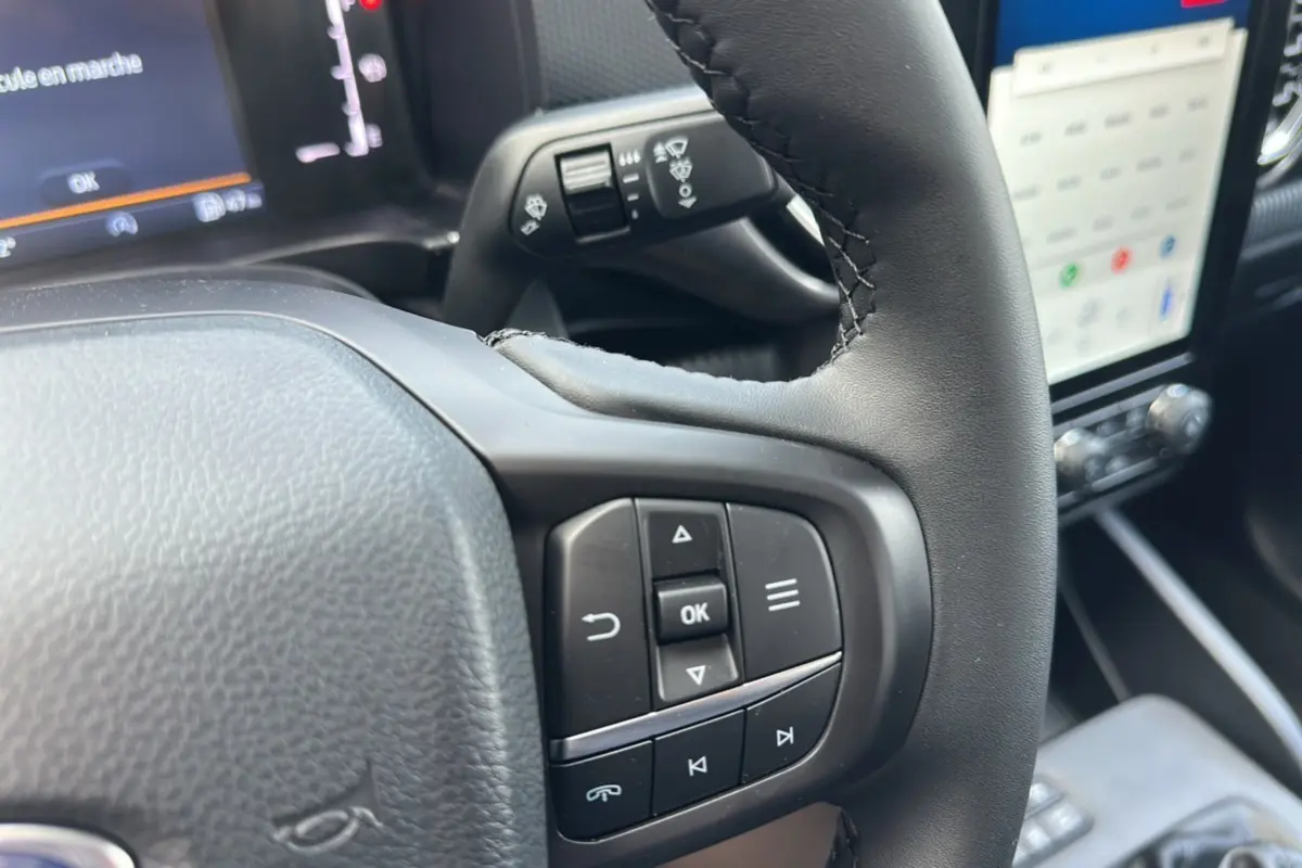 Gros plan sur le volant cuir multifonctions du Ford Ranger gris iconic, avec commandes intégrées et écran tactile en arrière-plan.
