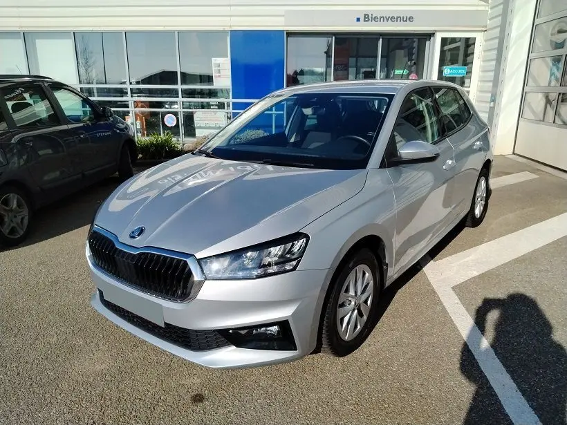 Vue 3/4 avant droite d'une Skoda Fabia blanche 2023, avec calandre noire et phares LED, stationnée devant un bâtiment.