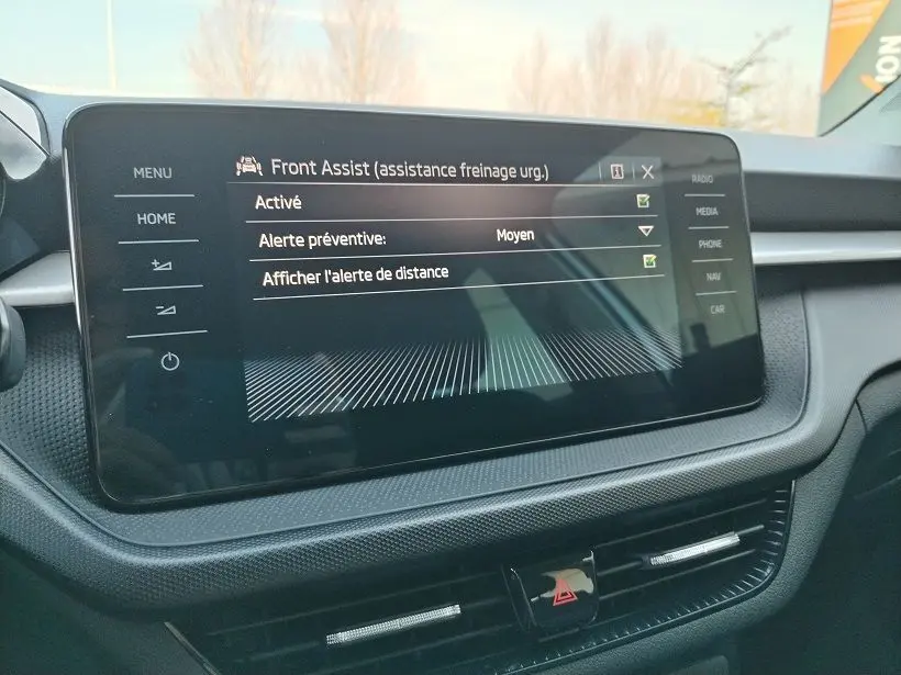 Écran tactile central du tableau de bord de la Skoda Fabia 2023 affichant les réglages de l'assistance freinage d'urgence Front Assist.