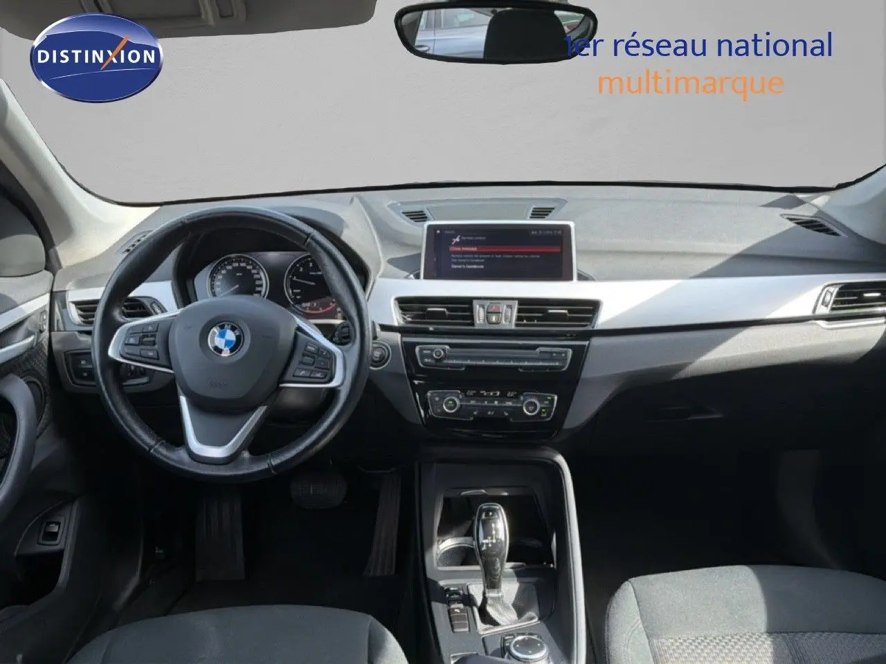 Intérieur de BMW X1 blanc 2022 vu de face, tableau de bord moderne avec écran central et volant multifonction.