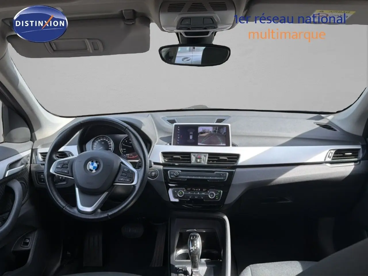 Vue intérieure avant du BMW X1 blanc 2022, tableau de bord moderne avec écran central et volant multifonction.