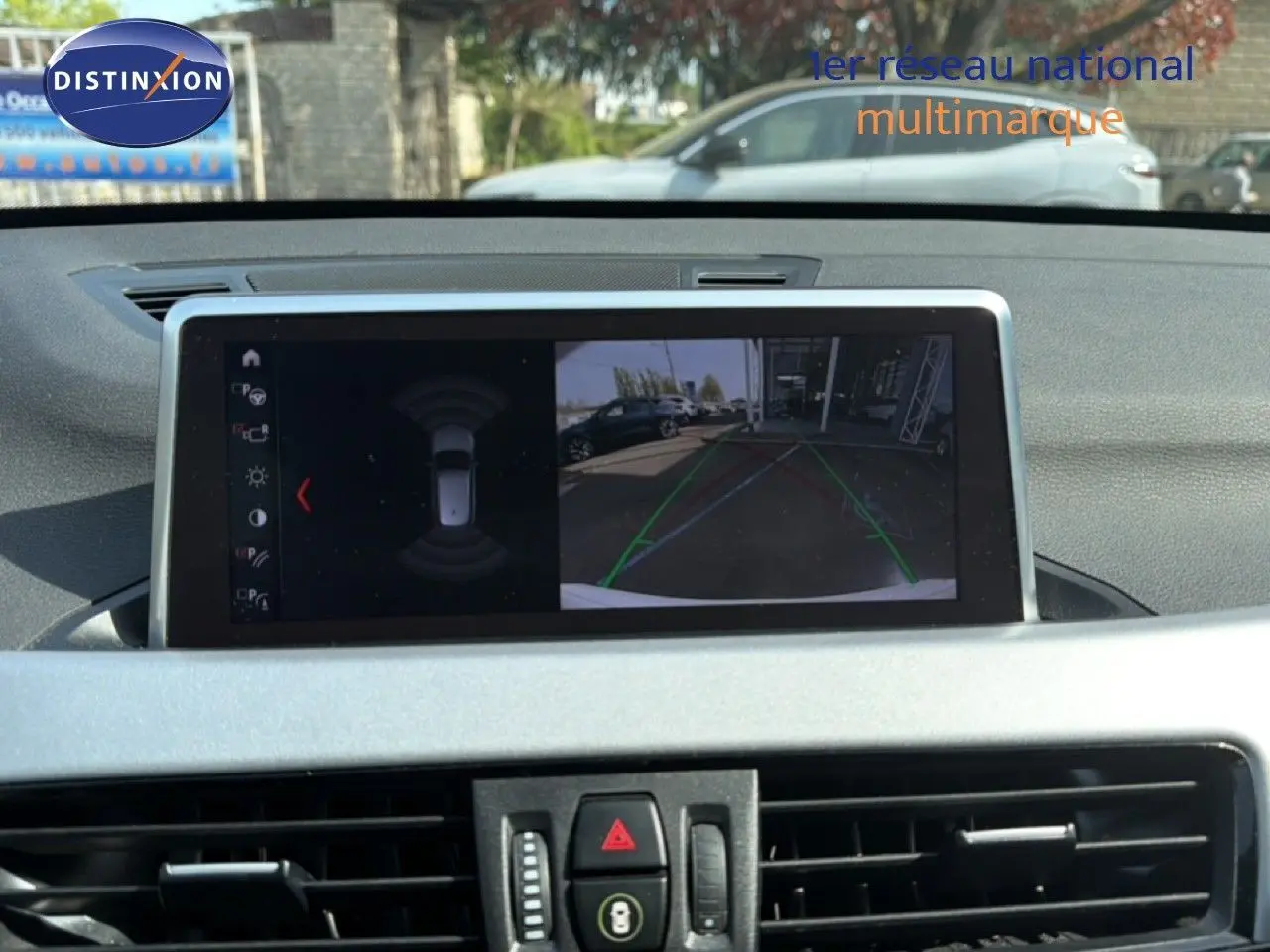 Écran central de BMW X1 blanc 2022 montrant la caméra de recul avec lignes de guidage en extérieur.