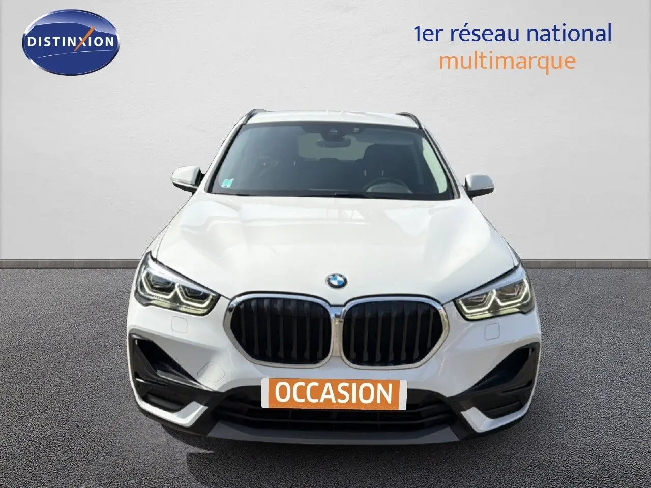 Vue frontale d'un BMW X1 blanc 2022 avec calandre noire et feux LED, sur fond neutre avec plaque "OCCASION".