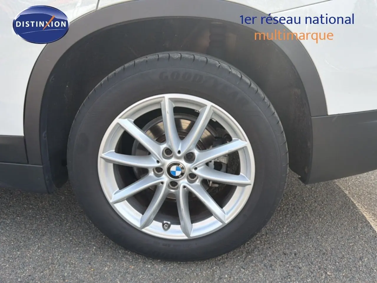 Gros plan sur la roue avant droite d’un BMW X1 blanc, avec jante alliage argentée à dix branches.