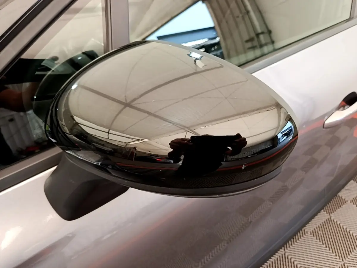 Gros plan sur le rétroviseur droit noir brillant du Renault Captur gris foncé, avec reflet intérieur visible.