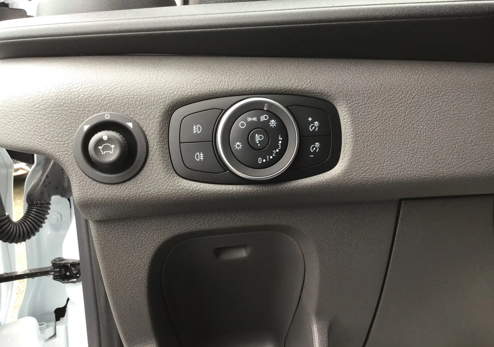 Détail du tableau de bord côté gauche du Ford Transit Fourgon blanc 2023 avec commandes d'éclairage et réglage des rétroviseurs.