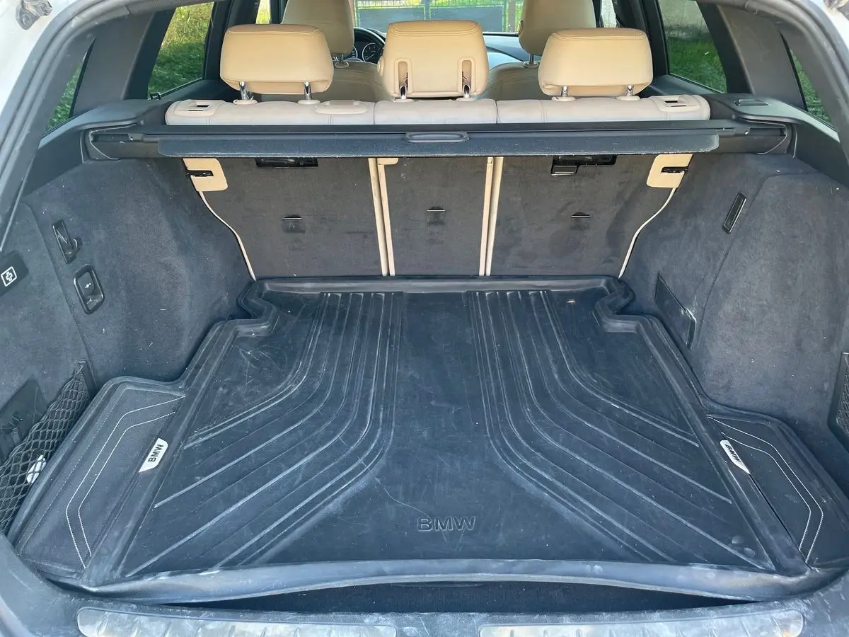 Coffre ouvert d'une BMW Série 3 Touring F31 blanc, vue arrière montrant le tapis de coffre noir avec logo BMW.