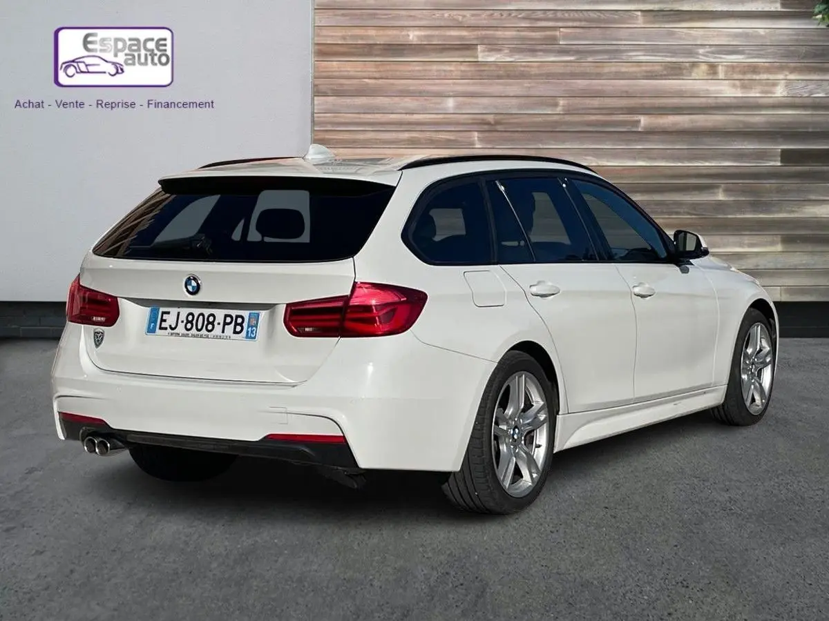 BMW Série 3 Touring F31 blanc vue 3/4 arrière droit avec double sortie d'échappement et vitres teintées.