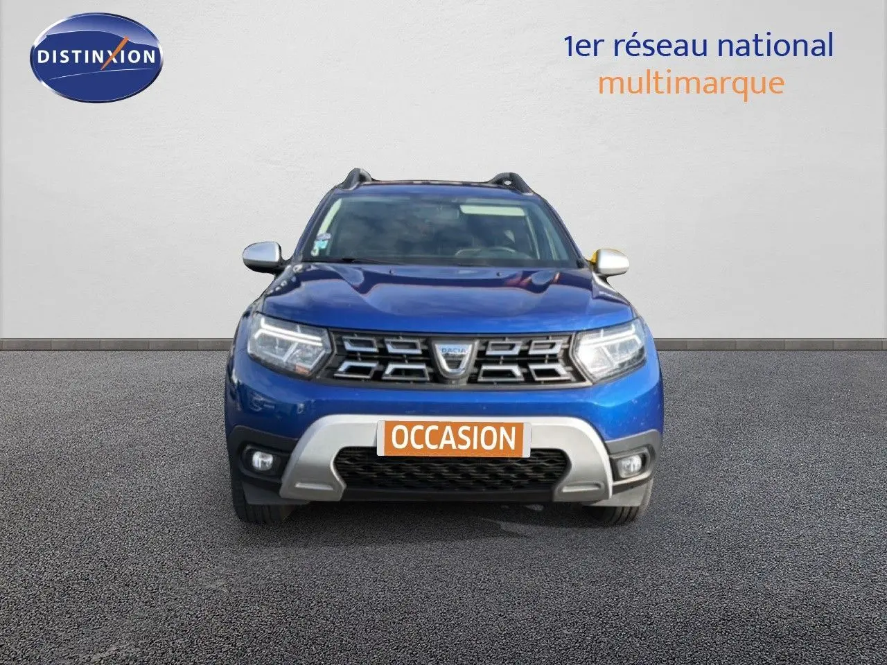 Vue frontale d'un Dacia Duster 2022 bleu Iron avec calandre chromée et plaque "OCCASION" visible.