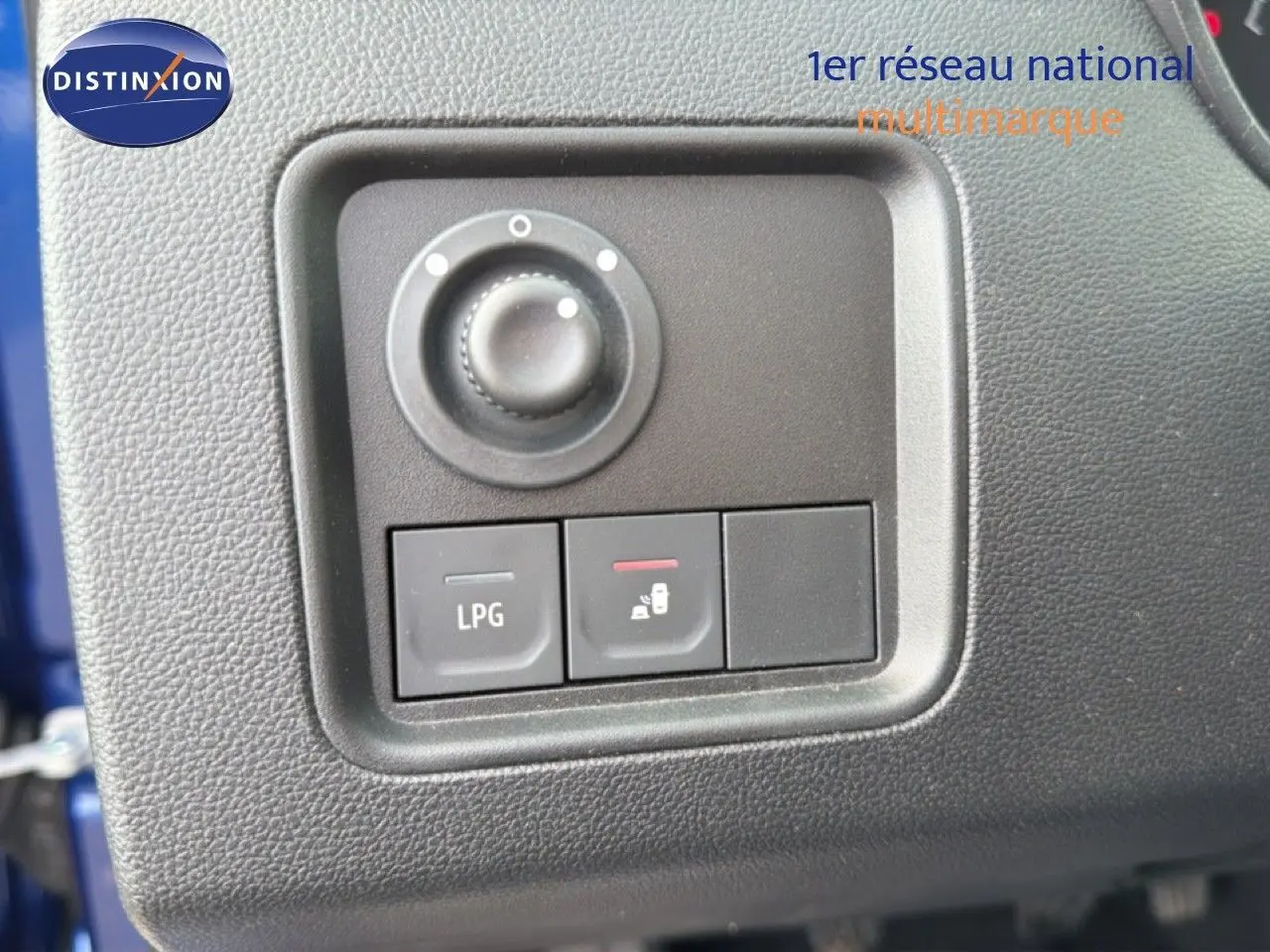Gros plan sur les commandes intérieures noires du tableau de bord du Dacia Duster bleu iron, avec bouton LPG visible.