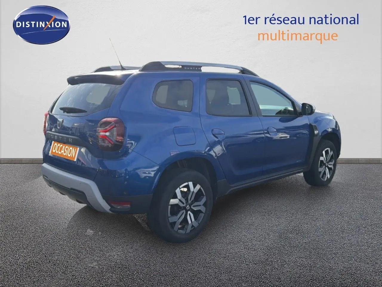 Vue 3/4 arrière droite d'un Dacia Duster 1.0 ECO-G 100 Prestige bleu Iron avec jantes bi-ton et barres de toit.