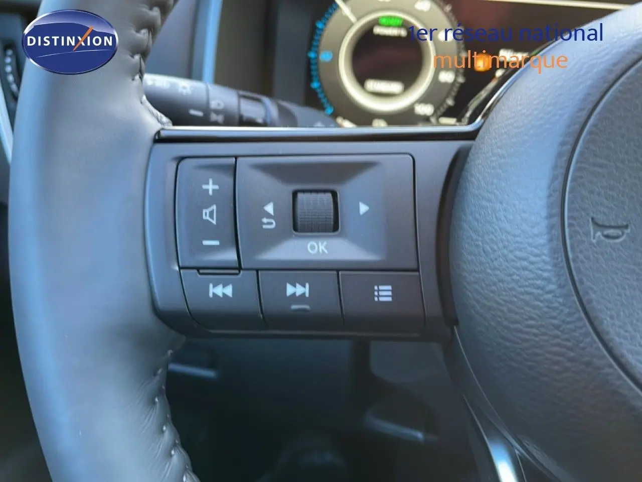 Gros plan sur les commandes au volant à gauche du Nissan Qashqai gris argile, avec tableau de bord numérique en arrière-plan flou.