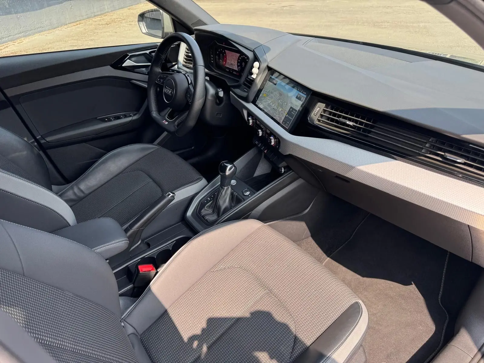 Vue intérieure côté conducteur de l'Audi A1 Sportback gris avec tableau de bord moderne et écran tactile GPS.