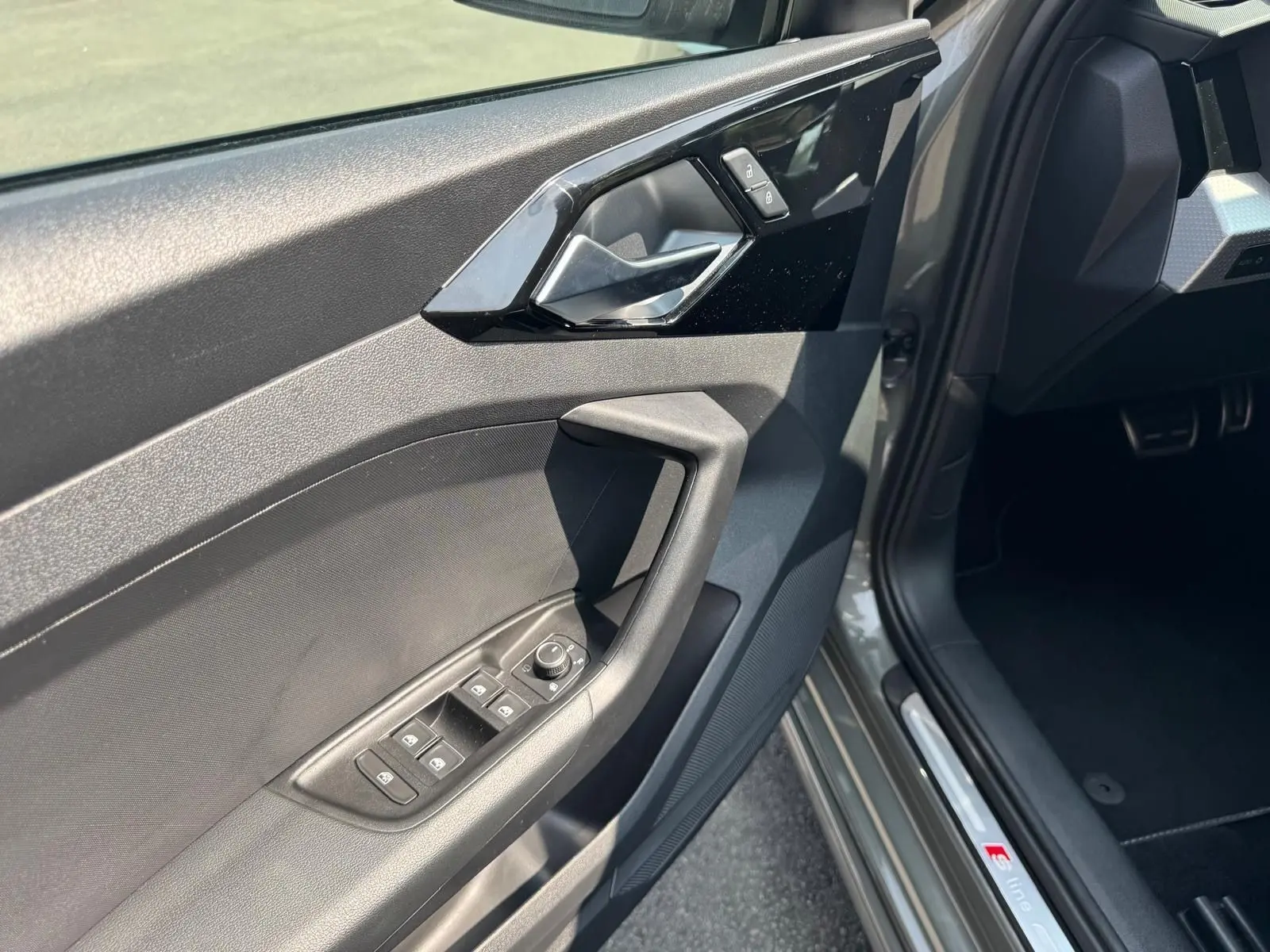 Gros plan sur la porte côté conducteur grise d'une Audi A1 Sportback 2019 avec commandes de vitres et badge S line.