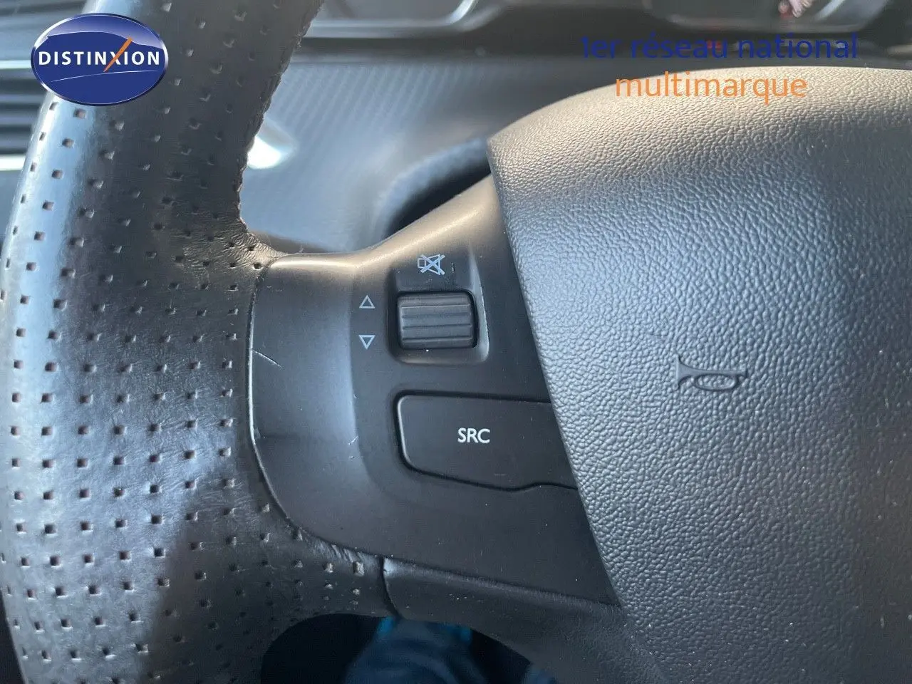 Gros plan sur le volant en cuir noir perforé du Peugeot 2008 gris platinium, avec commandes audio intégrées.