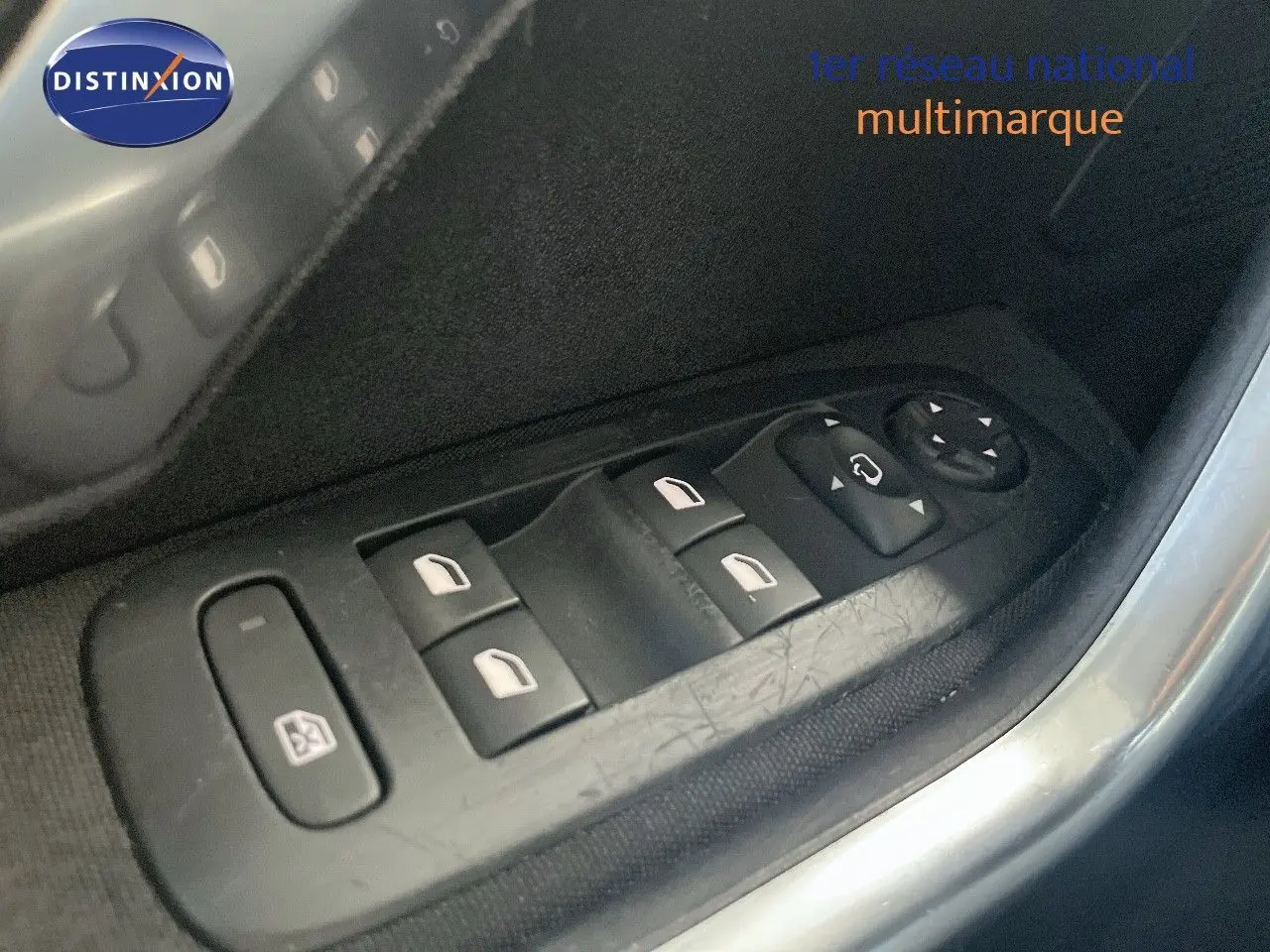 Gros plan sur les commandes des vitres électriques et des rétroviseurs côté conducteur d'une Peugeot 2008 gris platinium.