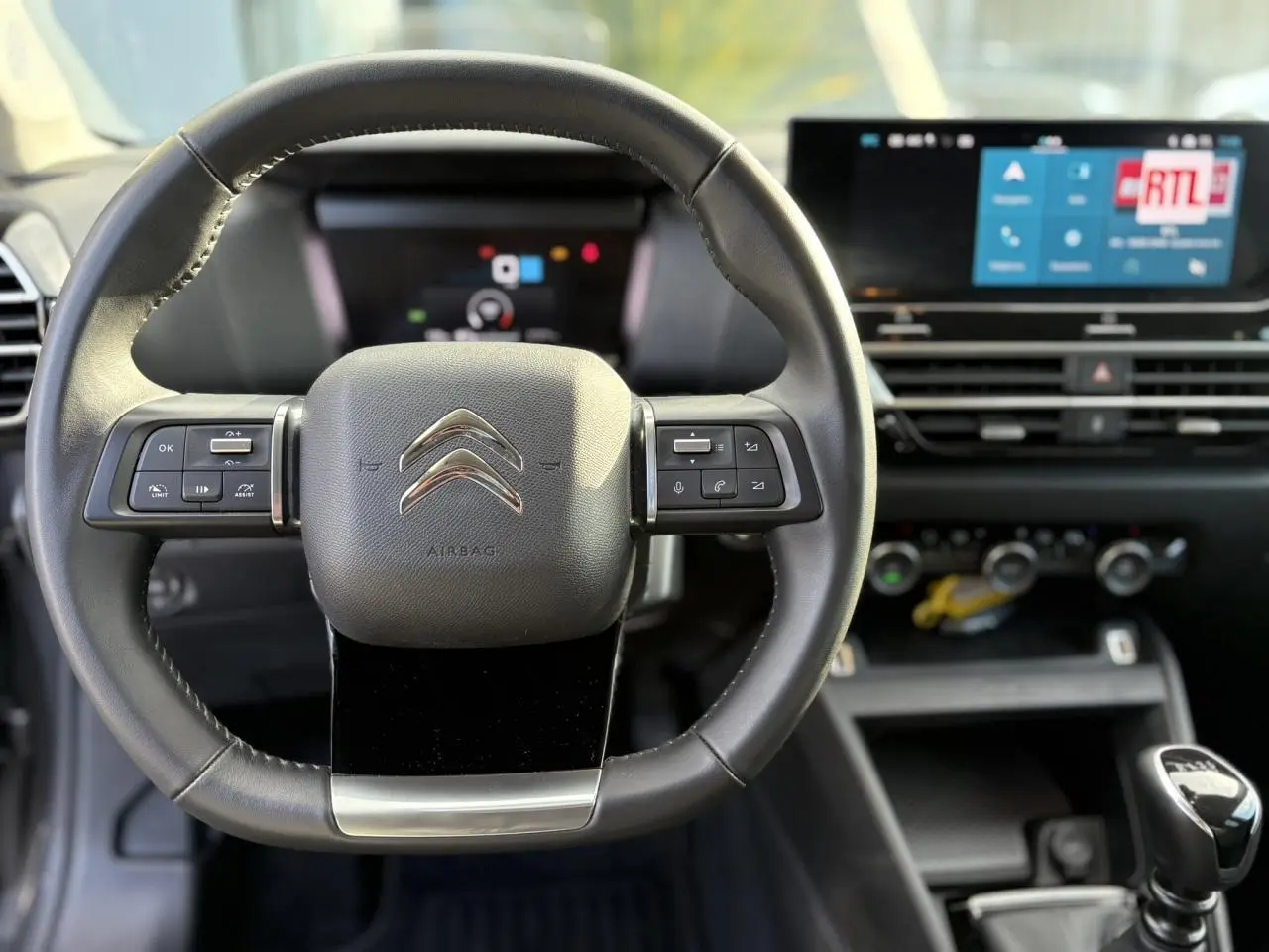 Vue intérieure centrée sur le volant cuir noir de la Citroën C4 2024 avec écran tactile et levier de vitesse manuel.