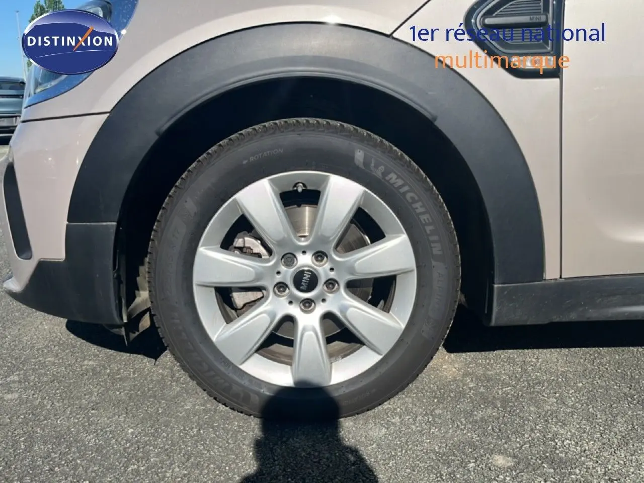 Gros plan sur la roue avant gauche d'une MINI Countryman grise avec jante alliage et logo MINI central visible.