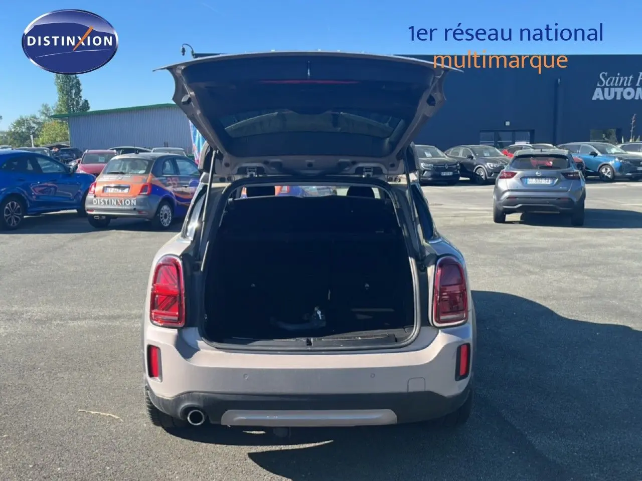 Vue arrière d'un MINI Countryman Cooper gris rooftop avec coffre ouvert sur un parking ensoleillé.