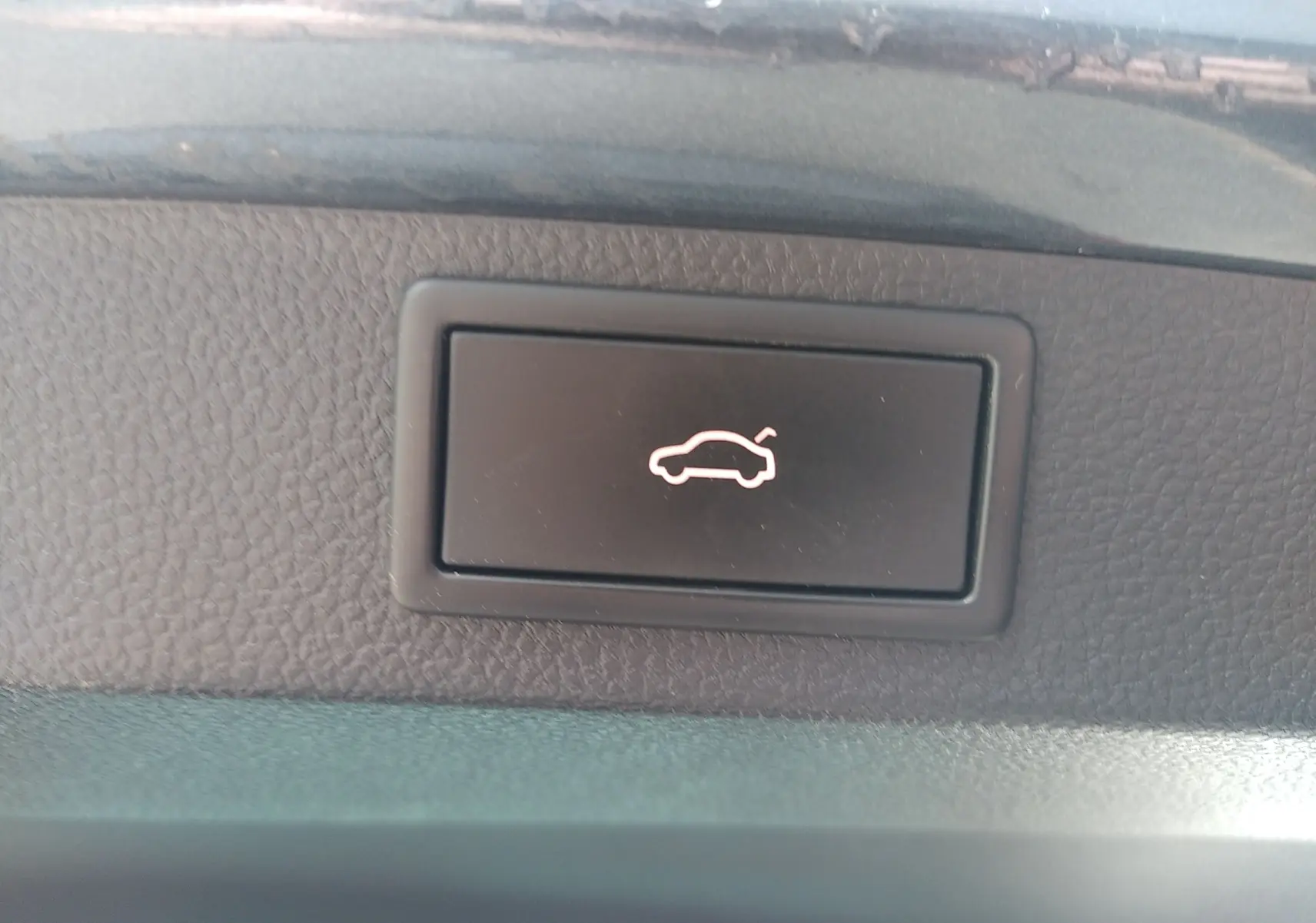 Bouton intérieur noir avec symbole lumineux blanc d'ouverture de coffre, sur Skoda Karoq gris, vue rapprochée du tableau de bord.