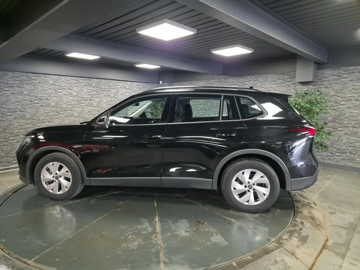 Vue de profil côté gauche d’un Volkswagen Tiguan noir 2025 avec jantes alliage 17 pouces dans un showroom.