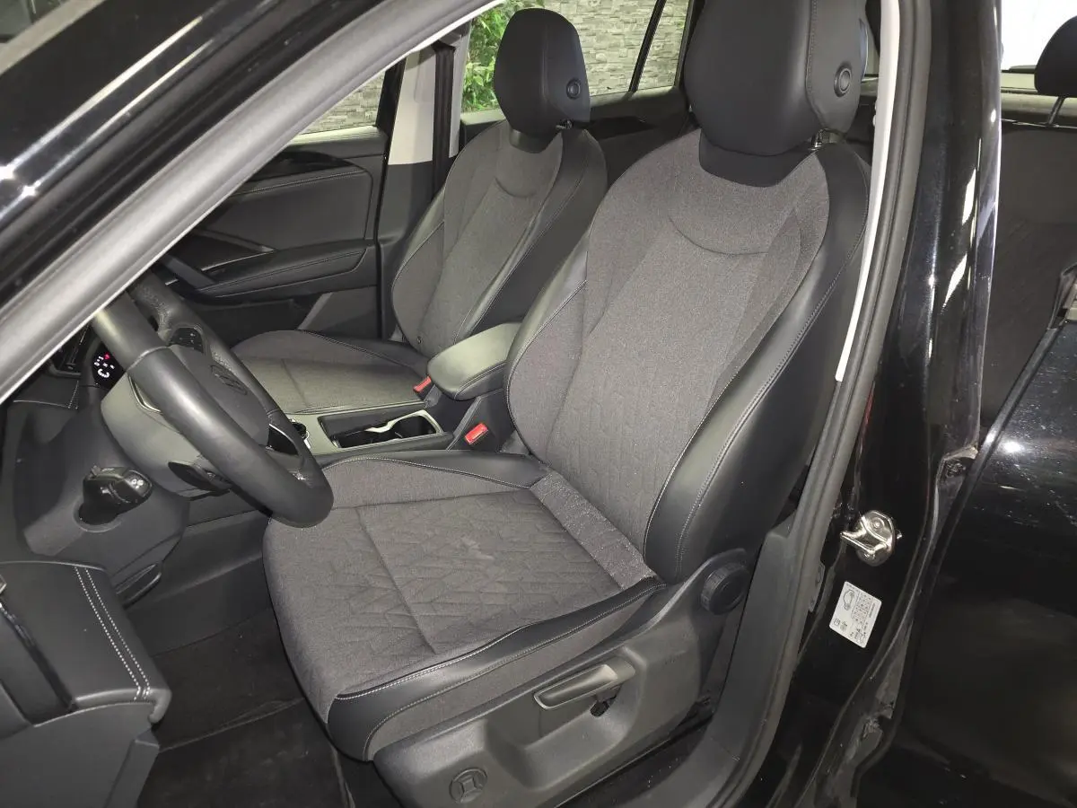 Vue intérieure côté conducteur du Volkswagen Tiguan noir 2025, sièges tissu et cuir gris avec accoudoir central.