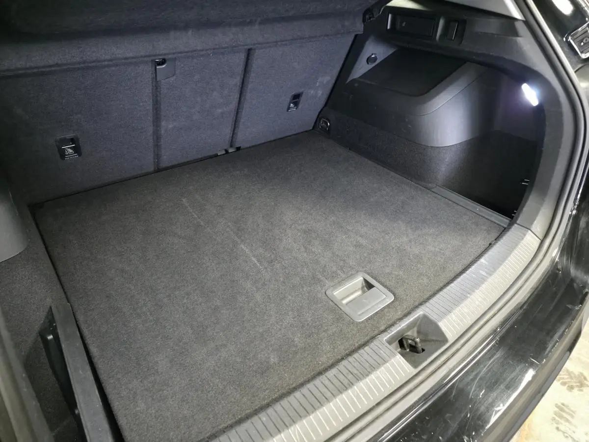 Coffre ouvert vu de côté droit, intérieur noir avec tapis de sol et éclairage LED, Volkswagen Tiguan noir 2025.