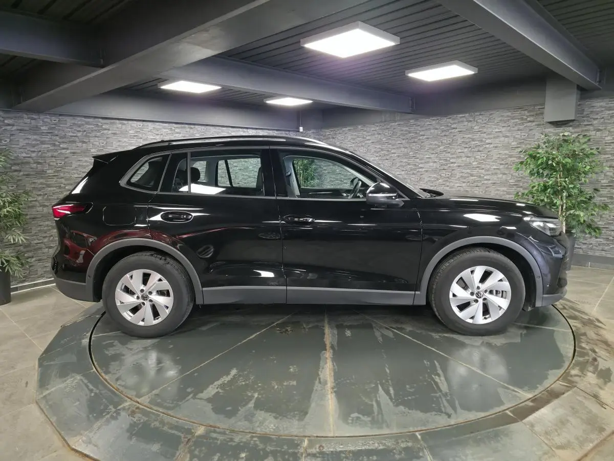 Vue de profil côté gauche d'un Volkswagen Tiguan noir 2025 avec jantes alliage 17 pouces dans un showroom intérieur.