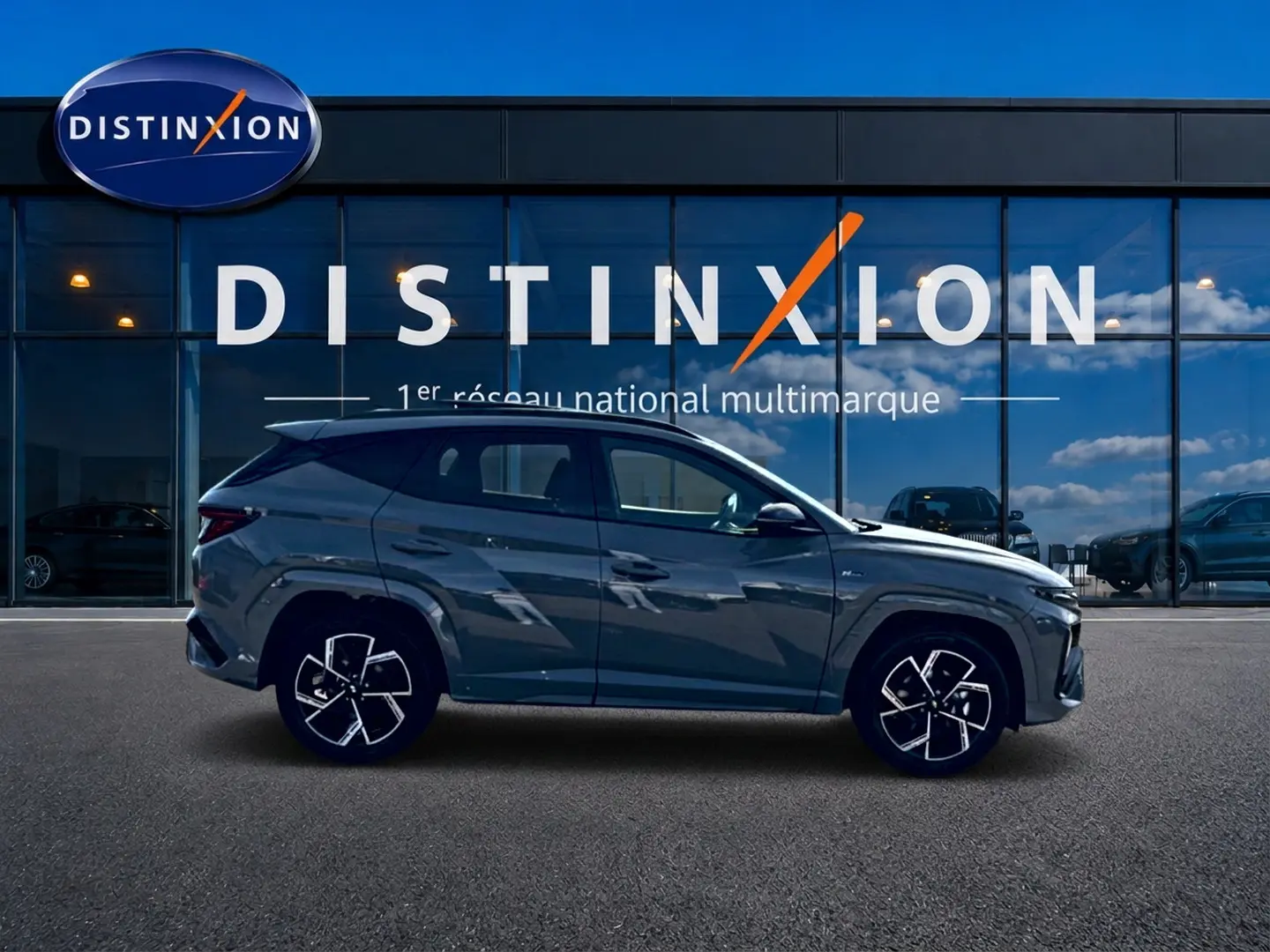 Hyundai Tucson 2026 gris shadow en profil droit devant une vitrine Distinxion, jantes alliage noires et chromées.