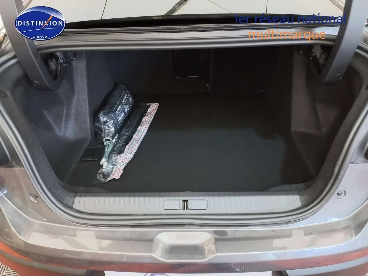 Coffre ouvert d'une Citroën C4 X gris platinium métal, montrant un espace de rangement propre avec kit de sécurité.