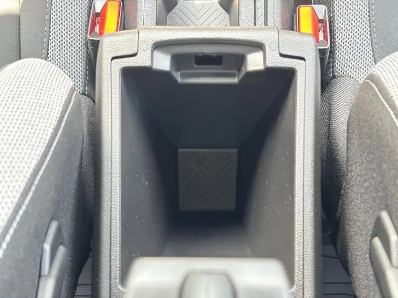 Vue plongeante sur le rangement central noir entre les sièges avant en tissu gris du Dacia Bigster blanc.
