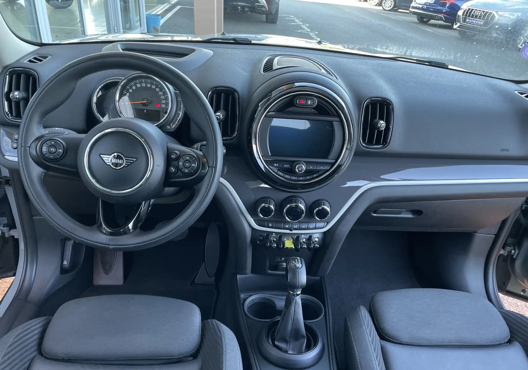 Vue intérieure avant du tableau de bord du MINI Countryman F60 hybride rechargeable en Moonwalk Grey, avec volant multifonction et écran central rond.