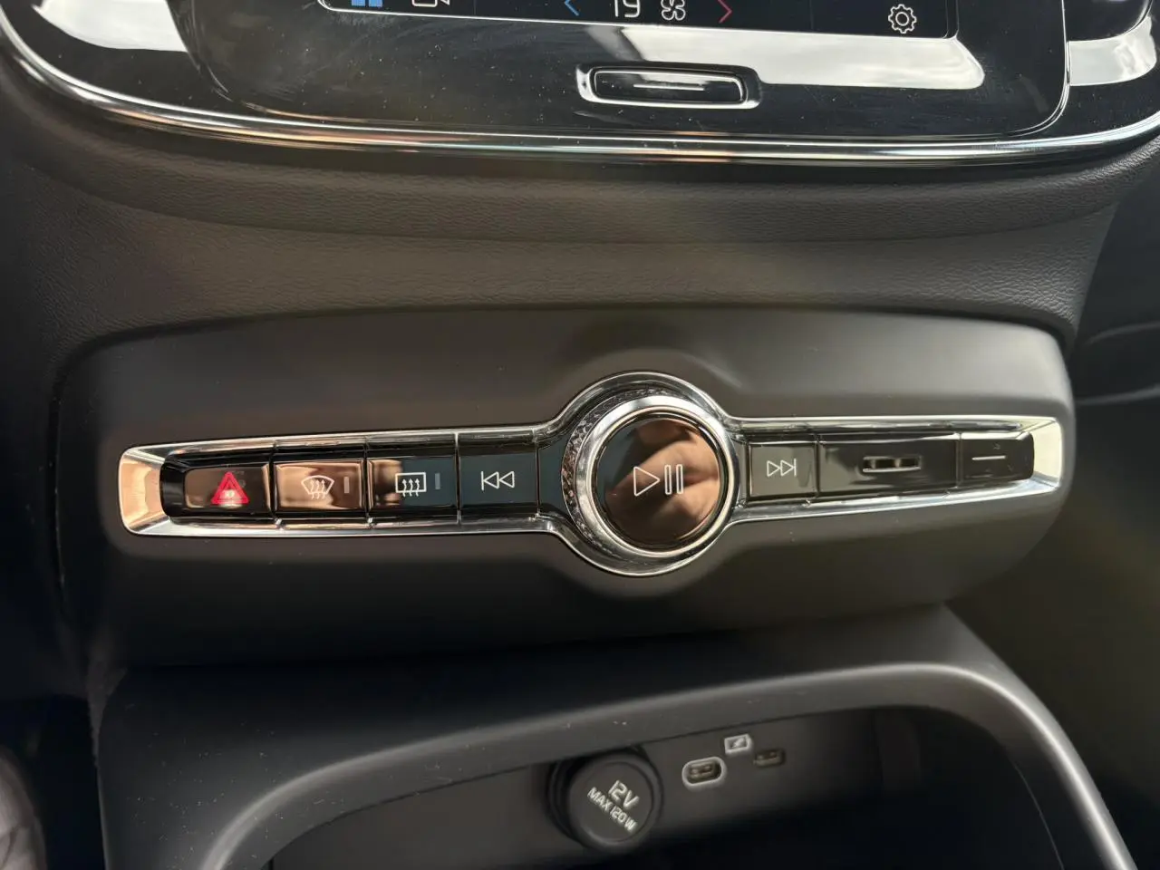 Vue rapprochée des commandes centrales noires et chromées du Volvo XC40 2024, mettant en valeur les boutons multimédia et de sécurité.