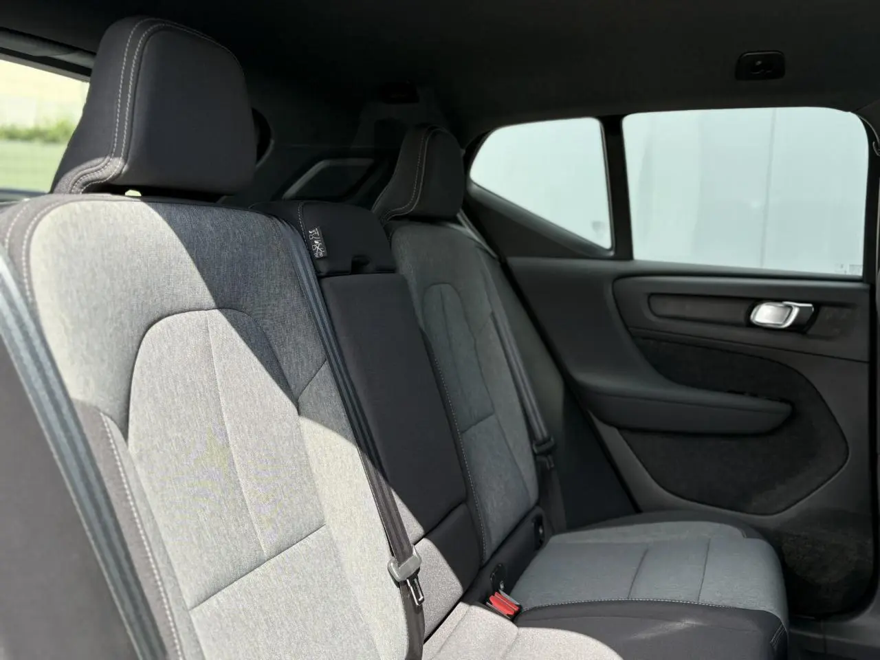 Vue latérale des sièges arrière gris clair du Volvo XC40 B3 MHEV 2024 avec garnitures noires et ceintures visibles.