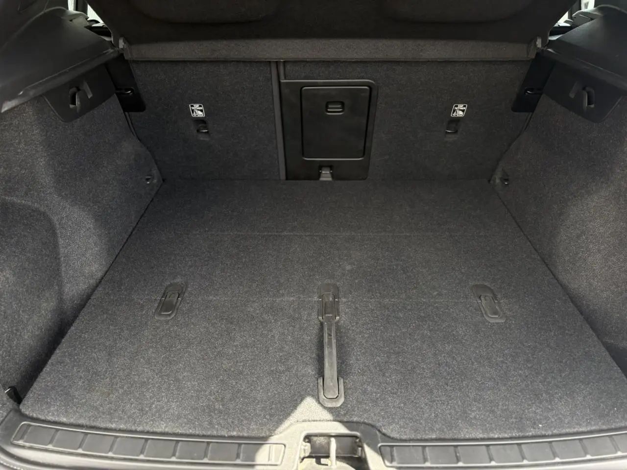 Coffre ouvert du Volvo XC40 B3 MHEV 2024, vue intérieure montrant le tapis gris et la trappe centrale.