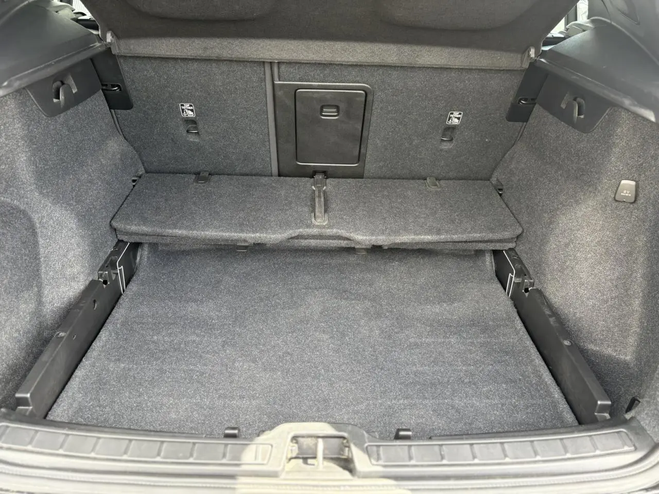 Coffre ouvert du Volvo XC40 B3 MHEV 2024, vue intérieure montrant le plancher et la cloison arrière en tissu gris.