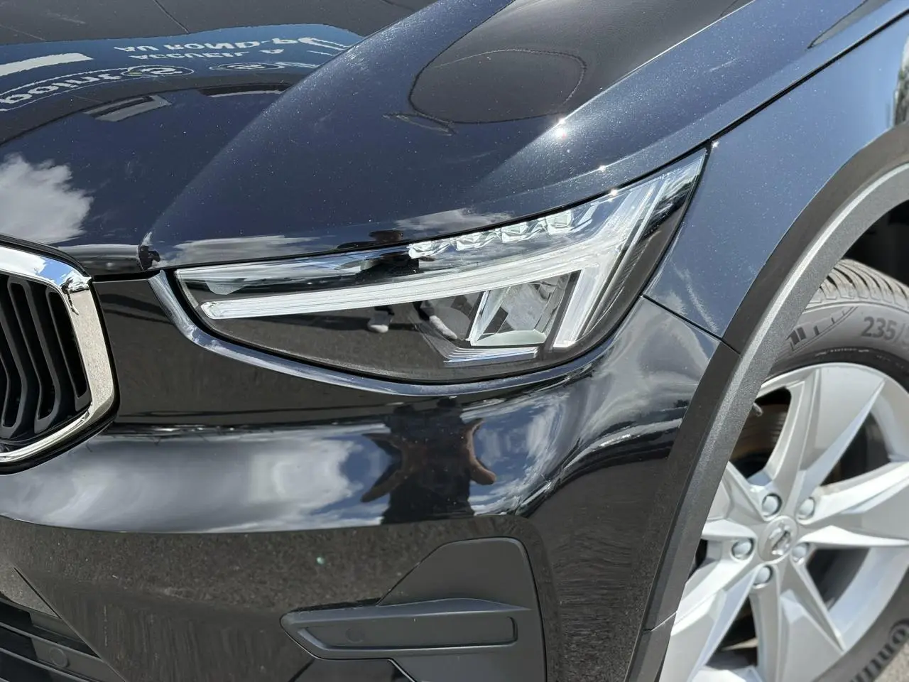 Gros plan sur le phare avant droit et la roue alliage 18'' d'un Volvo XC40 noir Onyx 2024.