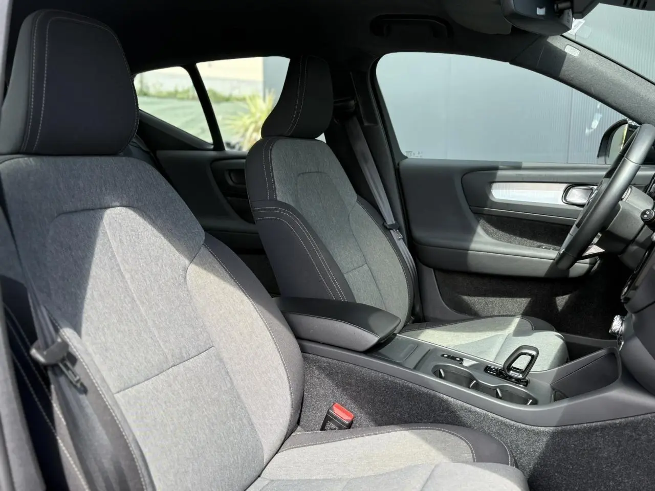 Intérieur du Volvo XC40 2024 vu côté conducteur, sièges tissu gris clair avec surpiqûres blanches et console centrale noire.