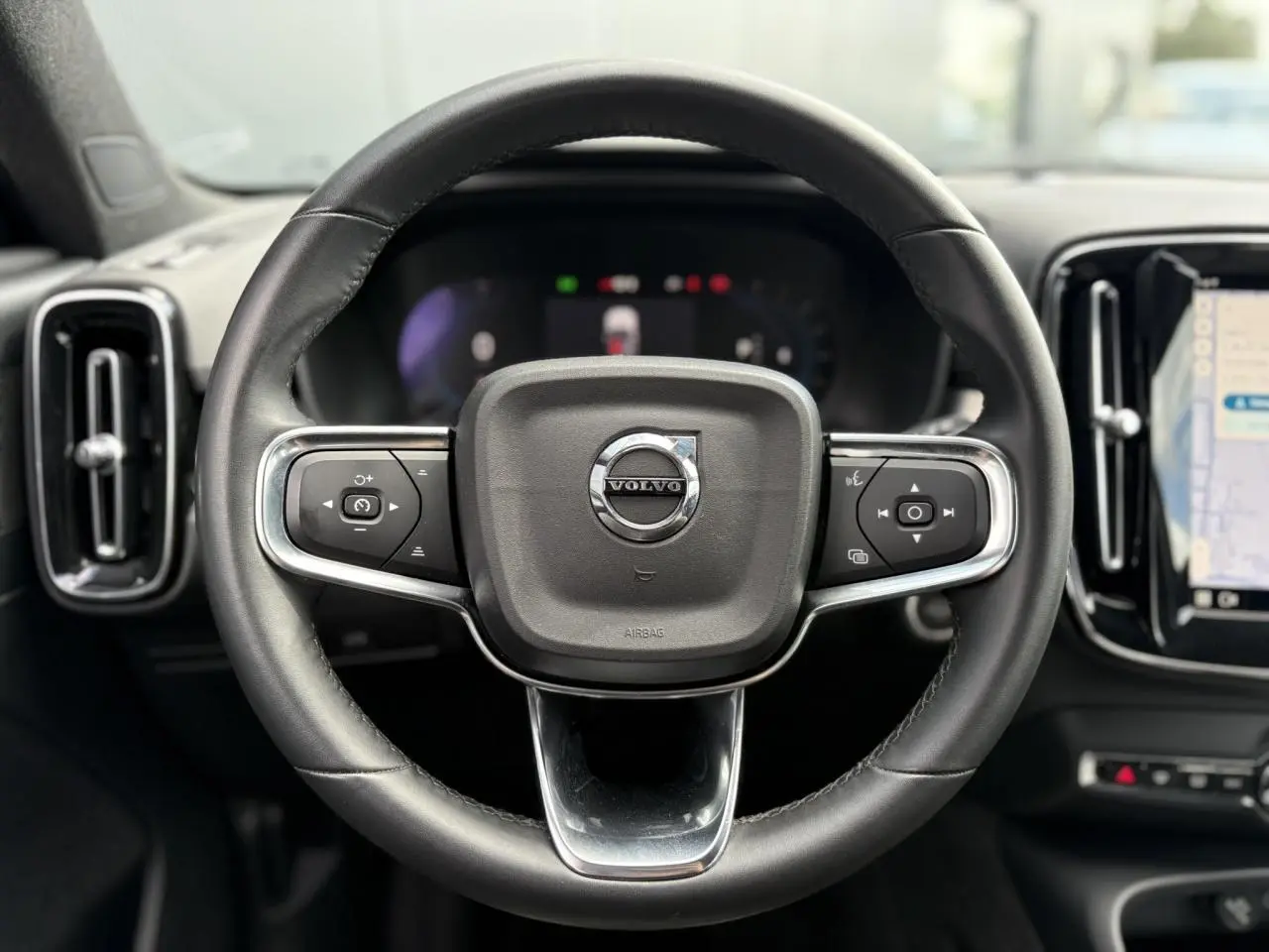 Volant cuir noir avec commandes intégrées du Volvo XC40 2024, tableau de bord et écran tactile visibles en arrière-plan.