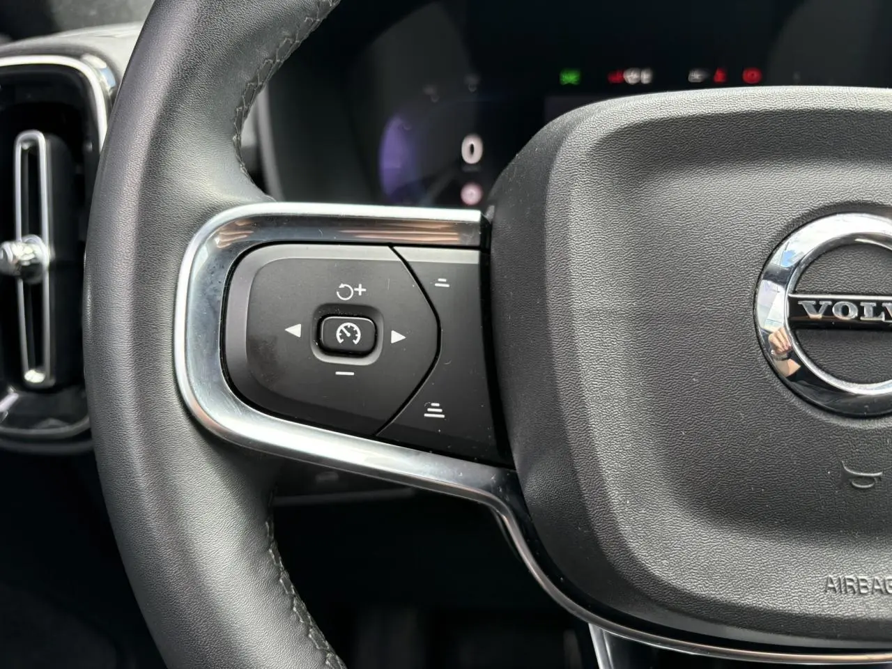 Gros plan sur le volant noir du Volvo XC40 2024, mettant en valeur les commandes de régulateur de vitesse côté gauche.