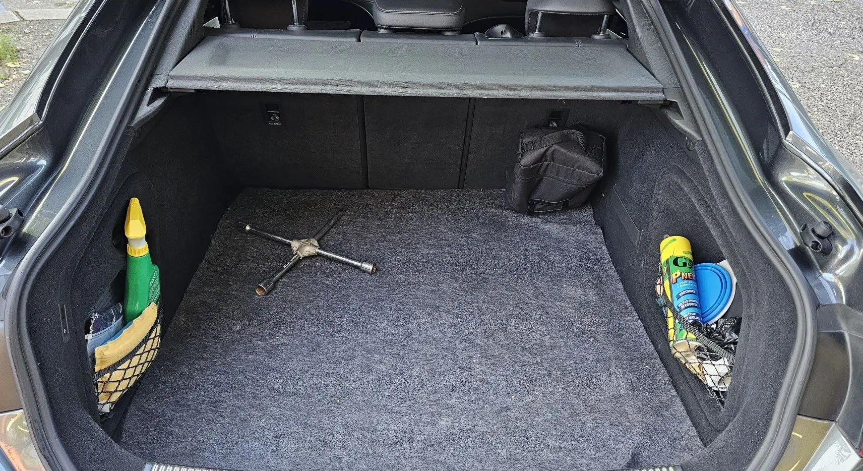 Coffre ouvert d'une Audi A5 Sportback gris Daytona, montrant un cric en croix et des accessoires de rangement latéraux.
