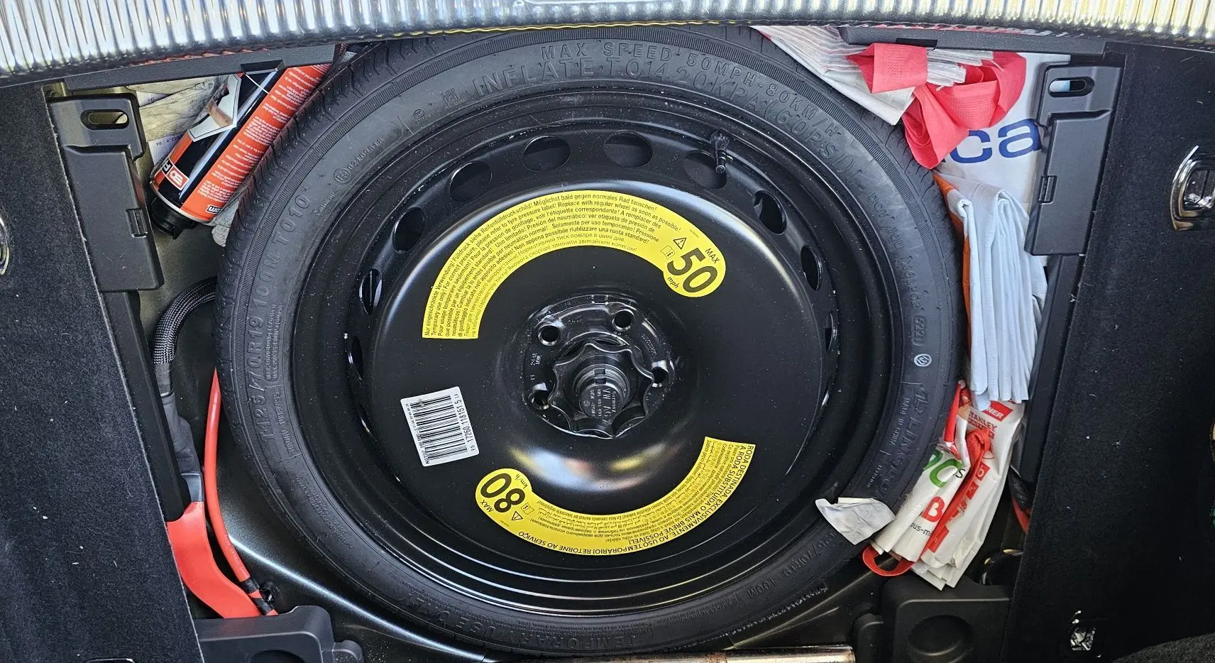 Roue de secours noire avec étiquettes jaunes visible dans le coffre d’une Audi A5 Sportback gris Daytona.