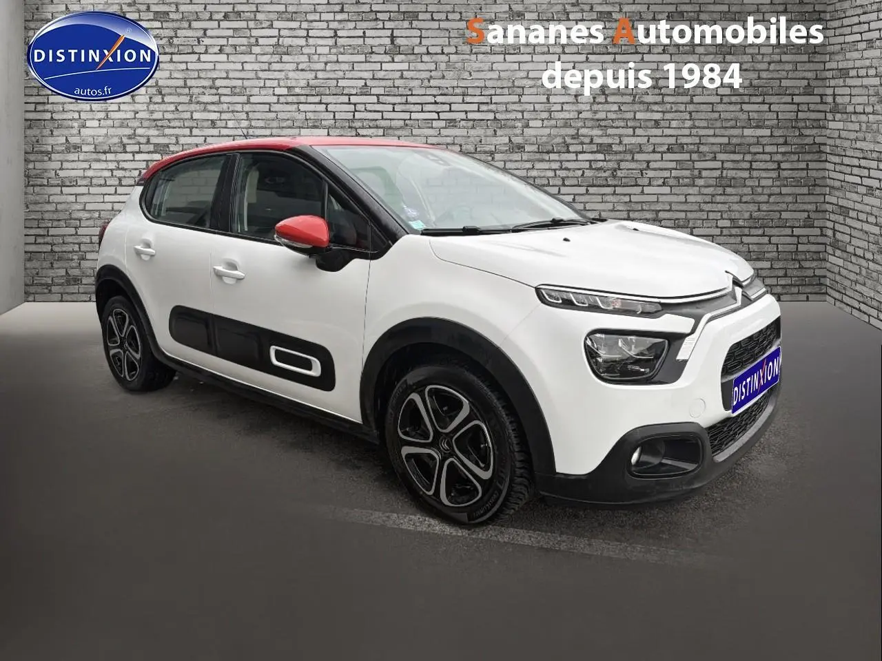 Citroën C3 blanc toit rouge vue 3/4 avant droit avec enjoliveurs noirs et rétroviseurs rouges.